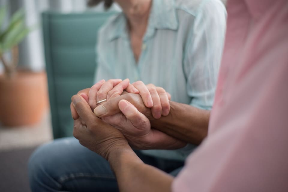 Een zorgmedewerker houdt de hand van een oudere vrouw vast